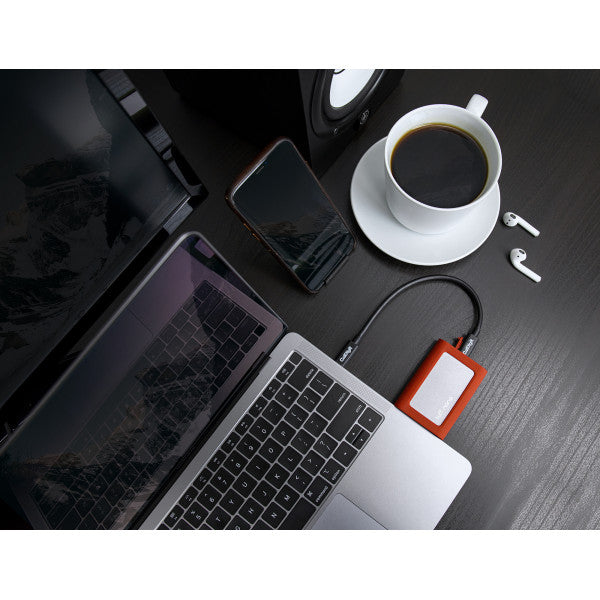 A desk with an Orange Tuff nano connected to a MacBook Pro, next to a cup of coffee, an iPhone, and Apple AirPods.